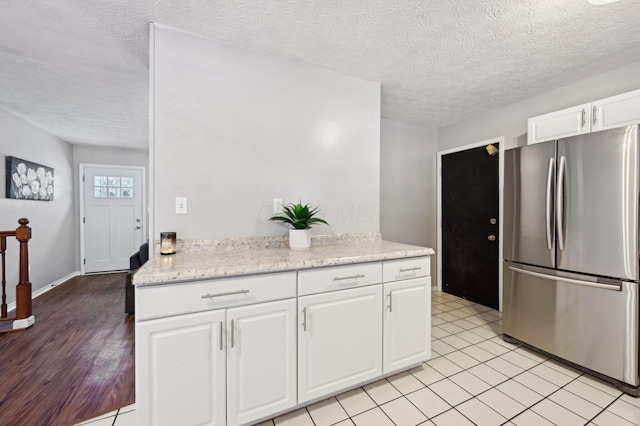 kitchen featuring light stone countertops, a textured ceiling, white cabinets, stainless steel refrigerator, and light tile patterned floors