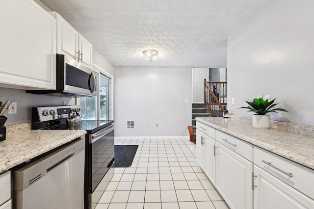 kitchen with light tile patterned floors, a textured ceiling, stainless steel appliances, and white cabinetry