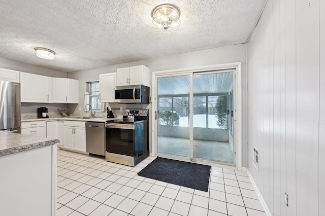 kitchen featuring light tile patterned floors, white cabinetry, wood walls, stainless steel appliances, and sink