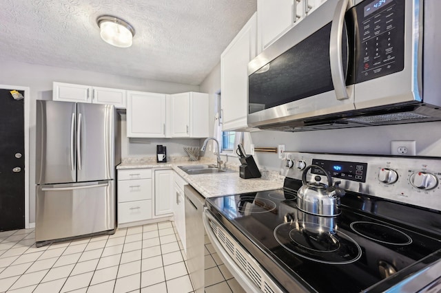 kitchen with light tile patterned floors, stainless steel appliances, a textured ceiling, white cabinets, and sink