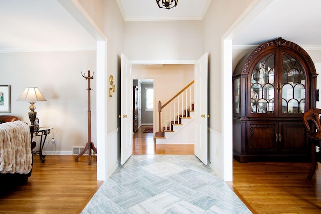 foyer entrance featuring ornamental molding, light wood-style flooring, stairway, and visible vents