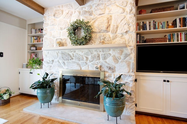 living area with a stone fireplace, light wood finished floors, beamed ceiling, and built in features