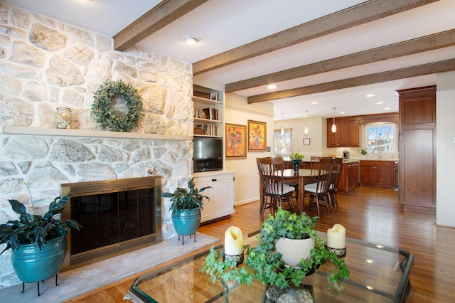 living room with a stone fireplace, beamed ceiling, light wood-type flooring, and recessed lighting