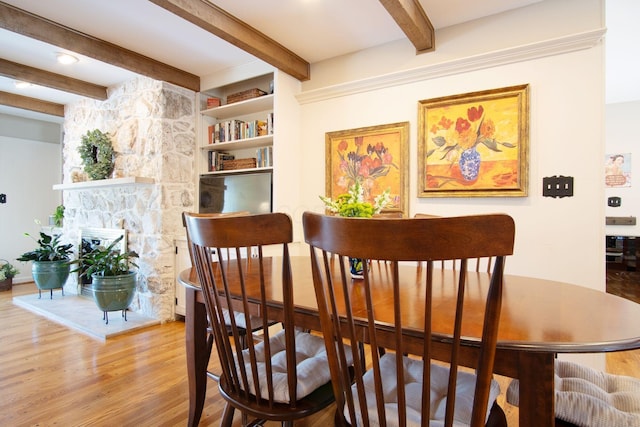 dining space with a fireplace, beam ceiling, and wood finished floors