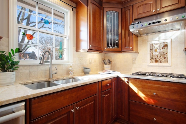 kitchen with glass insert cabinets, appliances with stainless steel finishes, light stone countertops, under cabinet range hood, and a sink