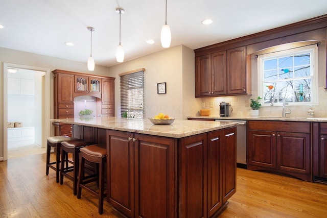 kitchen featuring light wood-style flooring, a breakfast bar, a center island, stainless steel dishwasher, and a sink