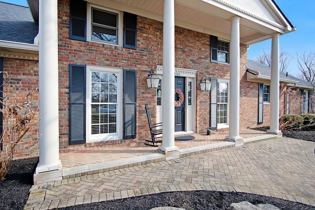 property entrance featuring a porch, roof with shingles, and brick siding