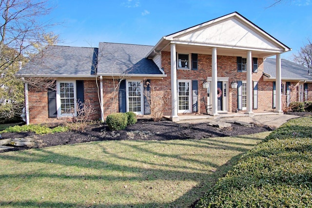 neoclassical home with a shingled roof, a front yard, and brick siding