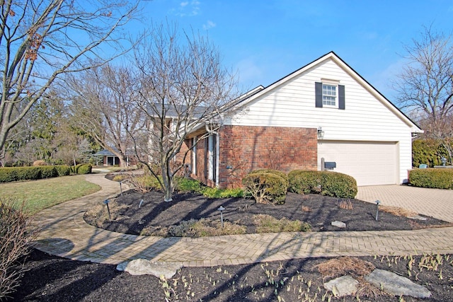 view of side of home with brick siding, decorative driveway, and an attached garage