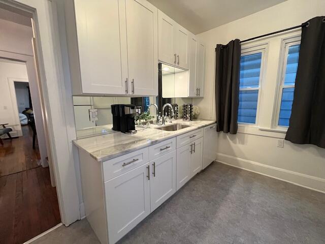 kitchen featuring light stone countertops, white cabinetry, and sink