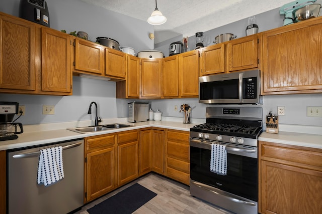 kitchen featuring a textured ceiling, decorative light fixtures, stainless steel appliances, light hardwood / wood-style floors, and sink