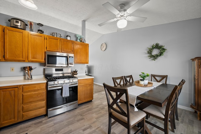 kitchen with lofted ceiling, light wood-type flooring, stainless steel appliances, and a textured ceiling