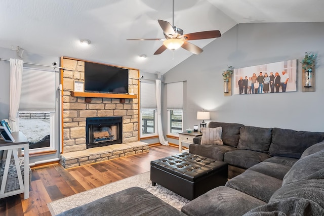 living room with vaulted ceiling, ceiling fan, hardwood / wood-style floors, and a stone fireplace