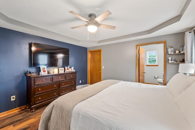 bedroom with ceiling fan, connected bathroom, dark hardwood / wood-style floors, and a tray ceiling