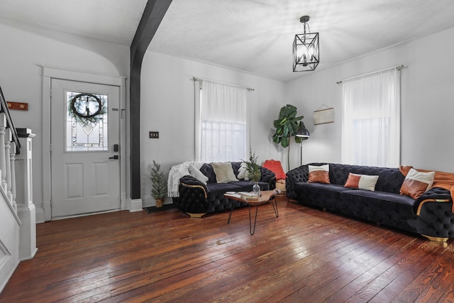 living room featuring beam ceiling, dark wood-type flooring, an inviting chandelier, and a textured ceiling