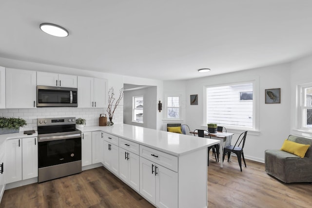 kitchen with white cabinetry, stainless steel appliances, dark hardwood / wood-style flooring, and kitchen peninsula