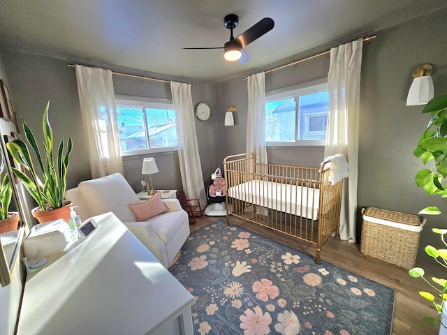 bedroom with ceiling fan, a crib, multiple windows, and hardwood / wood-style floors