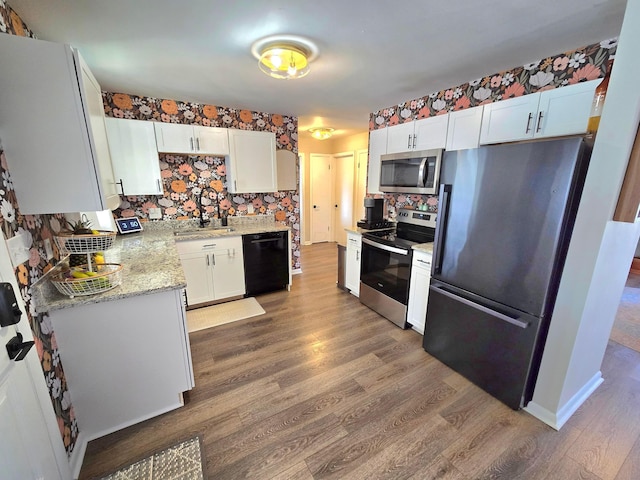 kitchen with hardwood / wood-style flooring, stainless steel appliances, backsplash, white cabinets, and light stone counters