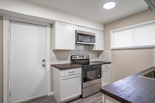 kitchen featuring wood counters, white cabinetry, wood finished floors, backsplash, and stainless steel appliances