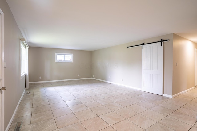 empty room featuring light tile patterned floors, baseboards, visible vents, and a barn door