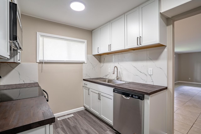 kitchen with a sink, butcher block countertops, decorative backsplash, white cabinets, and stainless steel dishwasher