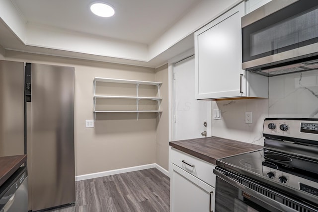 kitchen featuring white cabinetry, a raised ceiling, butcher block countertops, appliances with stainless steel finishes, and dark wood-style floors