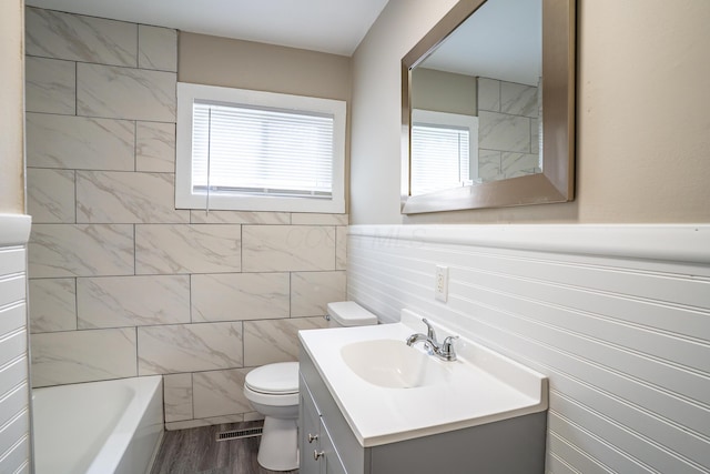 full bathroom with tile walls, toilet, wood finished floors, vanity, and visible vents