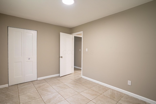 unfurnished bedroom featuring light tile patterned flooring, baseboards, and a closet