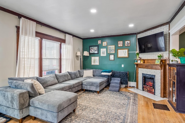 living room with wood-type flooring, a brick fireplace, and crown molding