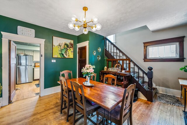 dining space featuring light hardwood / wood-style floors, a textured ceiling, and a notable chandelier