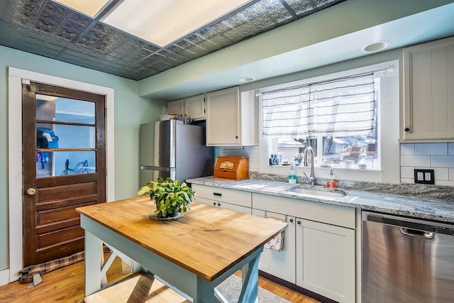 kitchen with light stone countertops, stainless steel appliances, sink, backsplash, and light wood-type flooring