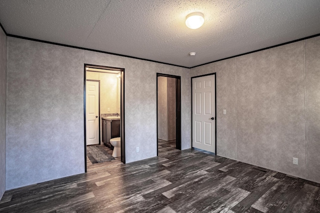 unfurnished bedroom with a textured ceiling, crown molding, dark hardwood / wood-style floors, and ensuite bath