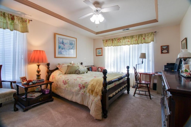 carpeted bedroom with a raised ceiling and ceiling fan