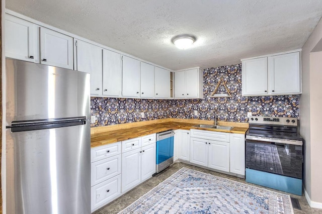 kitchen with butcher block countertops, sink, stainless steel appliances, and white cabinetry