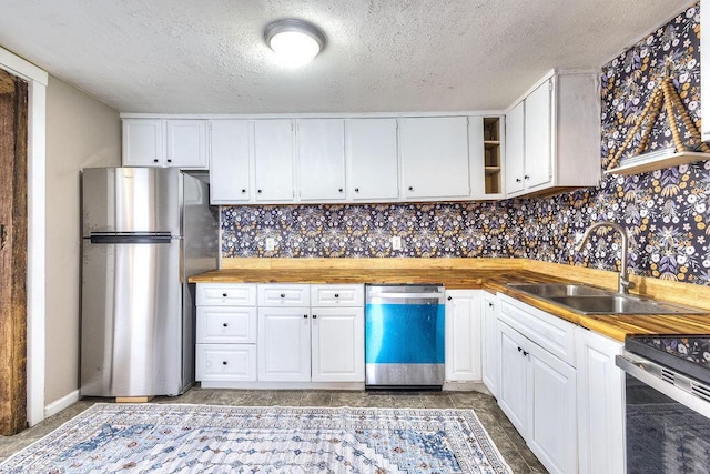 kitchen with tasteful backsplash, appliances with stainless steel finishes, white cabinetry, and butcher block countertops