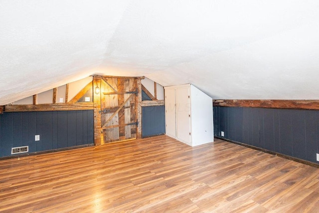 additional living space featuring wood-type flooring, lofted ceiling, and wood walls