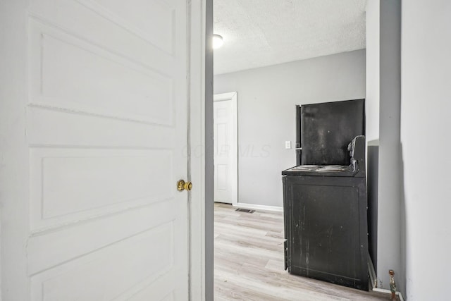 clothes washing area featuring washer / dryer, a textured ceiling, and light hardwood / wood-style flooring