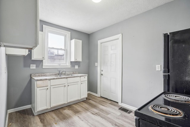 kitchen with a textured ceiling, sink, light hardwood / wood-style flooring, and white cabinets