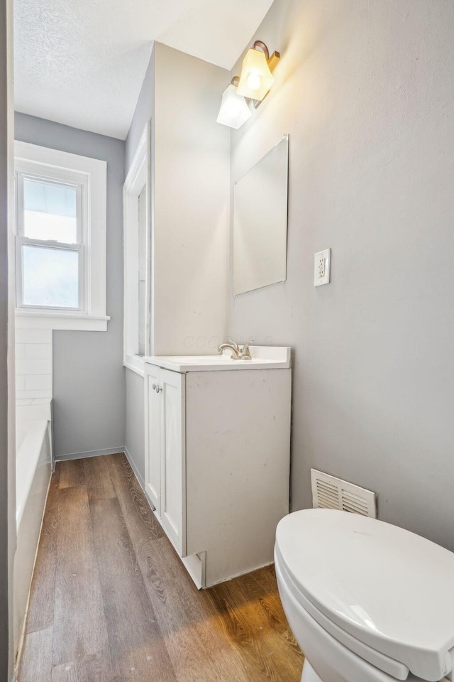 bathroom with hardwood / wood-style flooring, vanity, toilet, and a tub