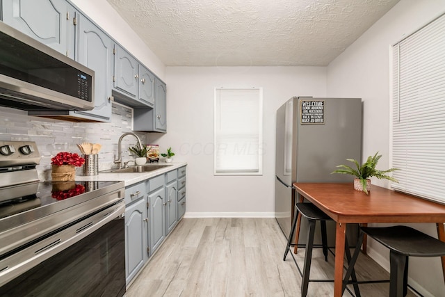 kitchen featuring sink, tasteful backsplash, a textured ceiling, appliances with stainless steel finishes, and light hardwood / wood-style floors