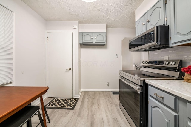 kitchen with gray cabinets, light wood-type flooring, backsplash, stainless steel appliances, and a textured ceiling