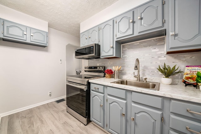 kitchen featuring sink, light hardwood / wood-style flooring, gray cabinets, appliances with stainless steel finishes, and decorative backsplash