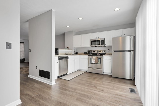 kitchen featuring light wood-type flooring, appliances with stainless steel finishes, and white cabinetry