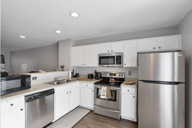 kitchen with kitchen peninsula, sink, appliances with stainless steel finishes, white cabinets, and dark hardwood / wood-style flooring