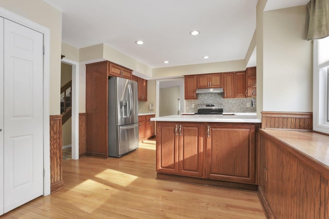 kitchen featuring stainless steel appliances, kitchen peninsula, decorative backsplash, and light hardwood / wood-style flooring