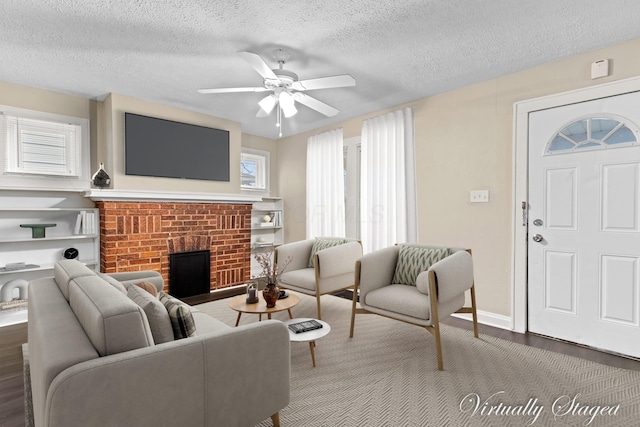 living room featuring ceiling fan, dark hardwood / wood-style flooring, a brick fireplace, and a textured ceiling