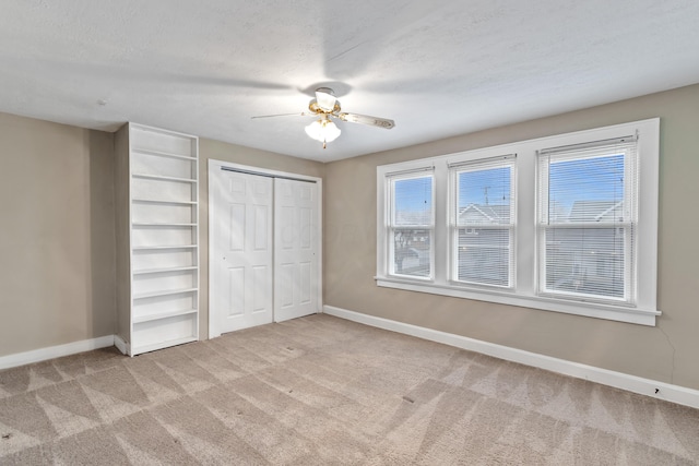 unfurnished bedroom featuring ceiling fan, a closet, light carpet, and a textured ceiling