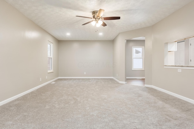 carpeted spare room featuring a textured ceiling, ceiling fan, and plenty of natural light