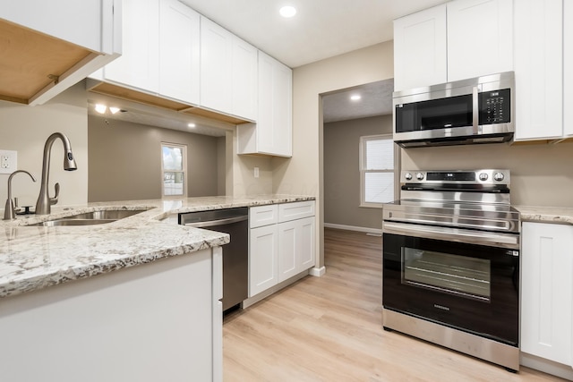 kitchen with light stone countertops, white cabinets, stainless steel appliances, light hardwood / wood-style floors, and sink