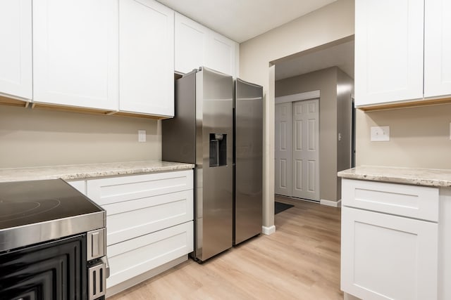 kitchen featuring light wood-type flooring, white cabinets, stainless steel fridge, and light stone countertops